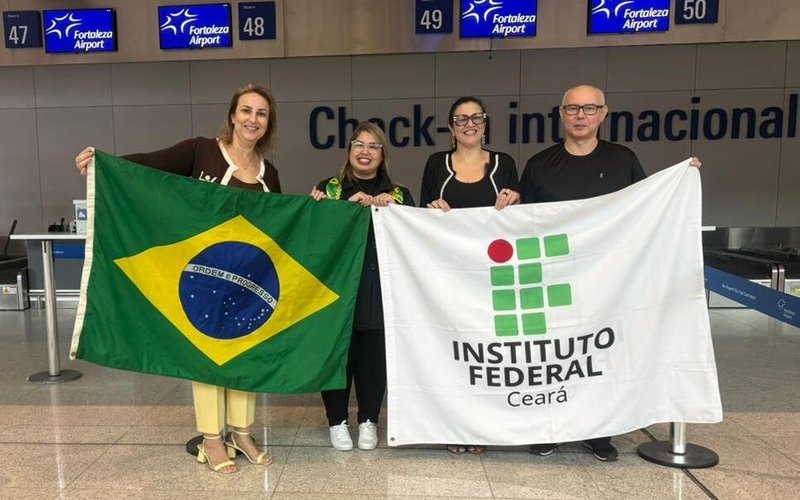 A imagem mostra a doutoranda Renata Teófilo de Sousa (ao centro) com os professores do IFCE, Ana Karine Portela e Auzuir Ripardo de Alexandria (ambos segurando a bandeira do IFCE) no aeroporto de Fortaleza antes do embarque da estudante para Macau, na China.